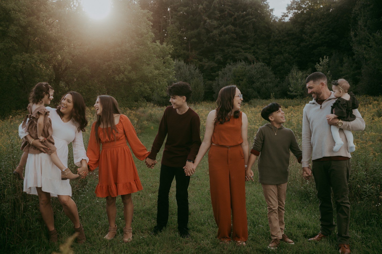 The Miller family of MBG Exteriors & More holding hands in a field at sunset