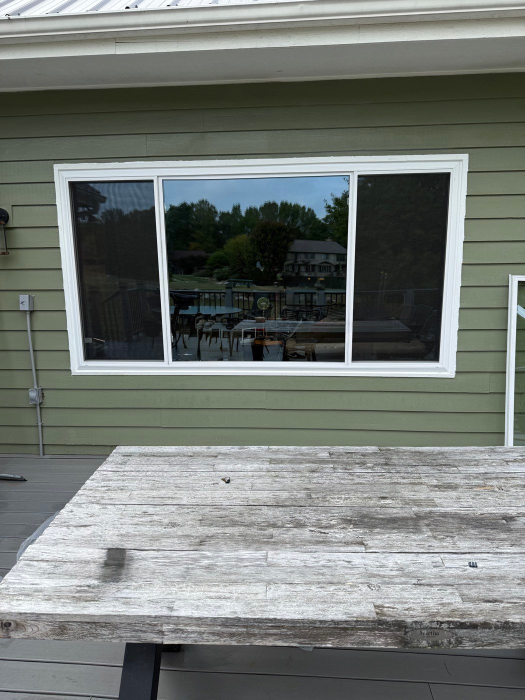 New white-framed picture window on a home with green siding
